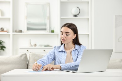 Photo of Budget planning. Beautiful young woman with papers and laptop at white table indoors