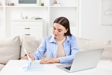 Photo of Budget planning. Beautiful young woman with papers and laptop at white table indoors