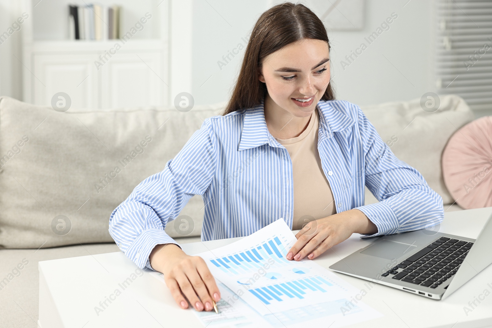 Photo of Budget planning. Young woman with papers and laptop at white table indoors