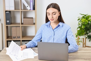 Photo of Budget planning. Beautiful young woman with papers and laptop at wooden table in office