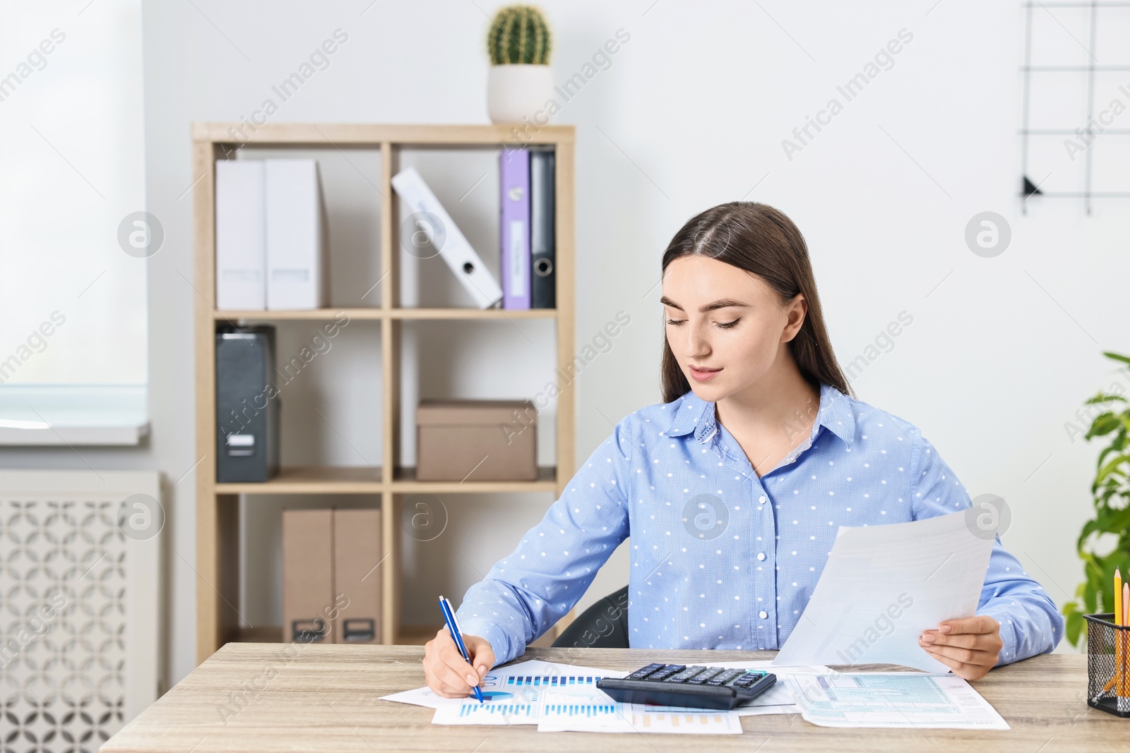 Photo of Budget planning. Beautiful young woman with papers and calculator at wooden table in office