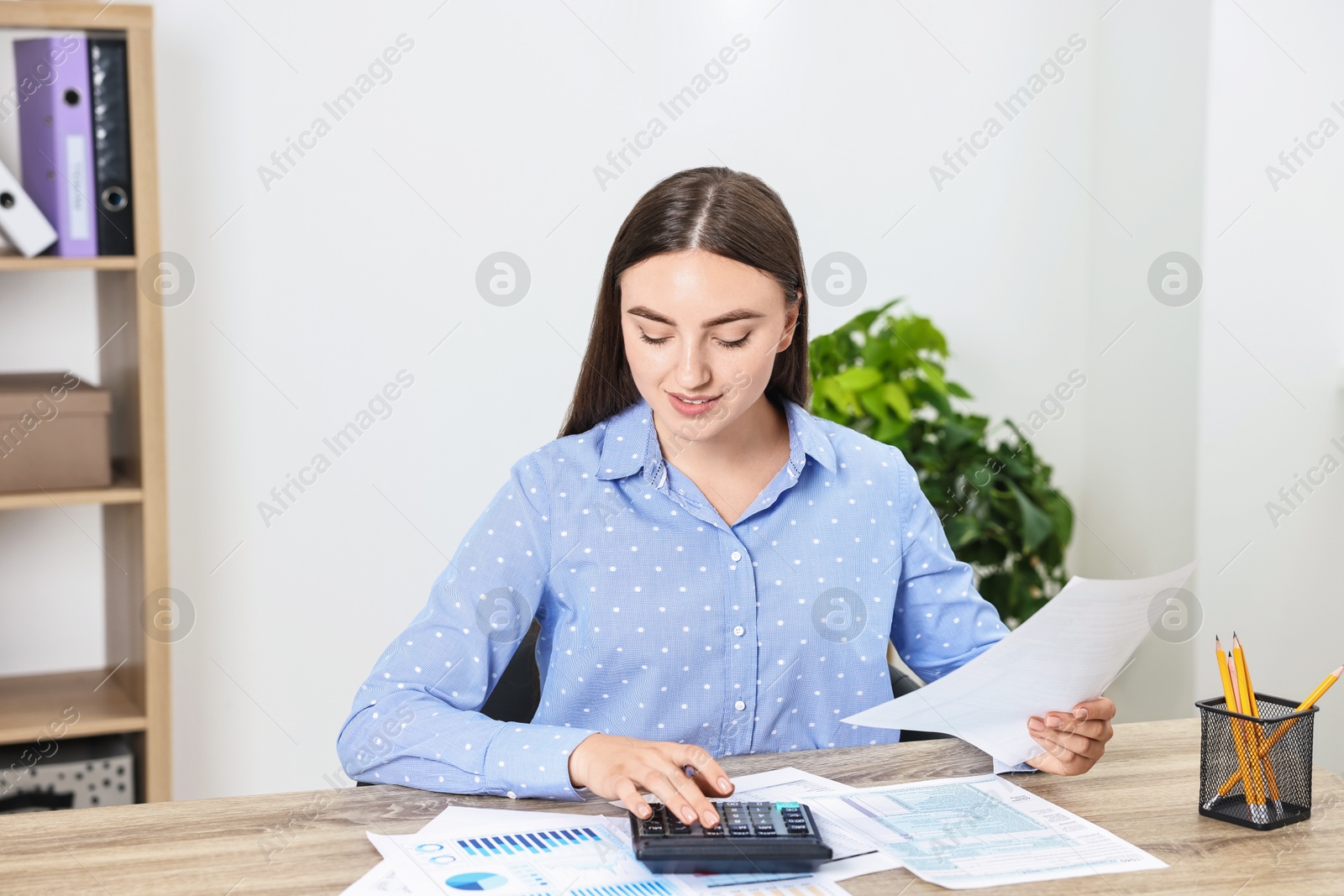 Photo of Budget planning. Beautiful young woman with papers using calculator at wooden table in office