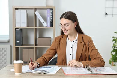 Budget planning. Beautiful young woman with papers and calculator at wooden table in office