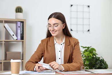 Photo of Budget planning. Young woman with papers using calculator at wooden table in office