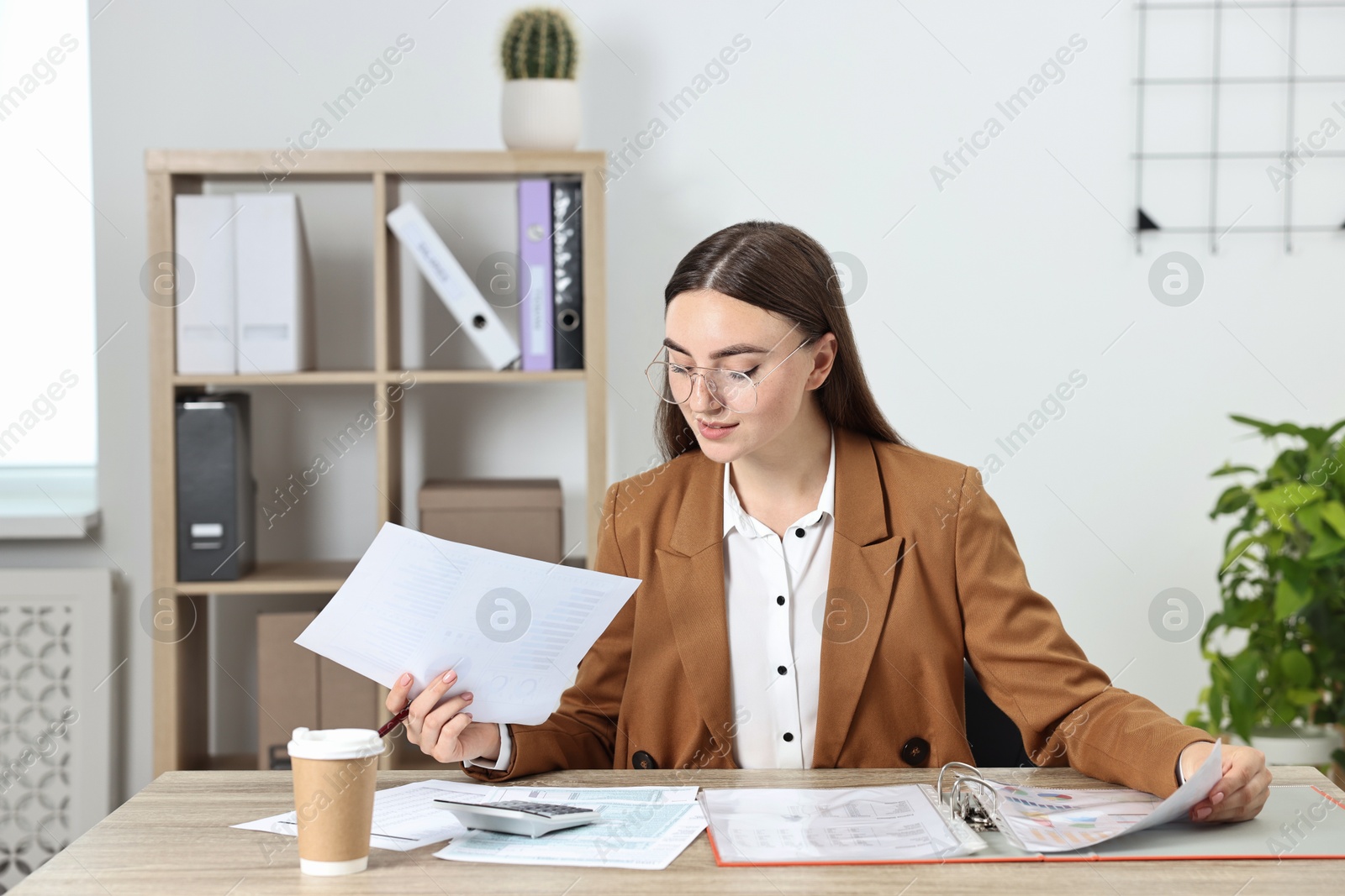 Photo of Budget planning. Beautiful young woman with papers and calculator at wooden table in office