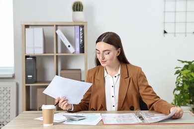 Budget planning. Beautiful young woman with papers and calculator at wooden table in office