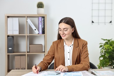 Photo of Budget planning. Beautiful young woman with papers and calculator at wooden table in office