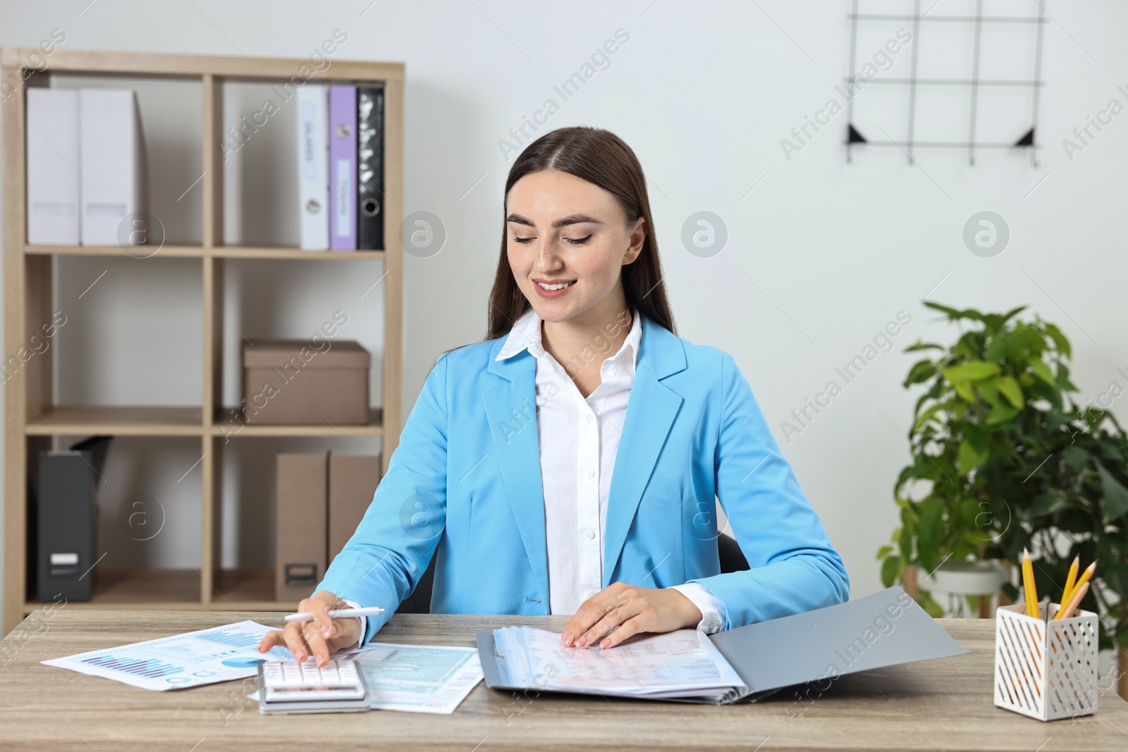 Photo of Budget planning. Young woman with papers using calculator at wooden table in office