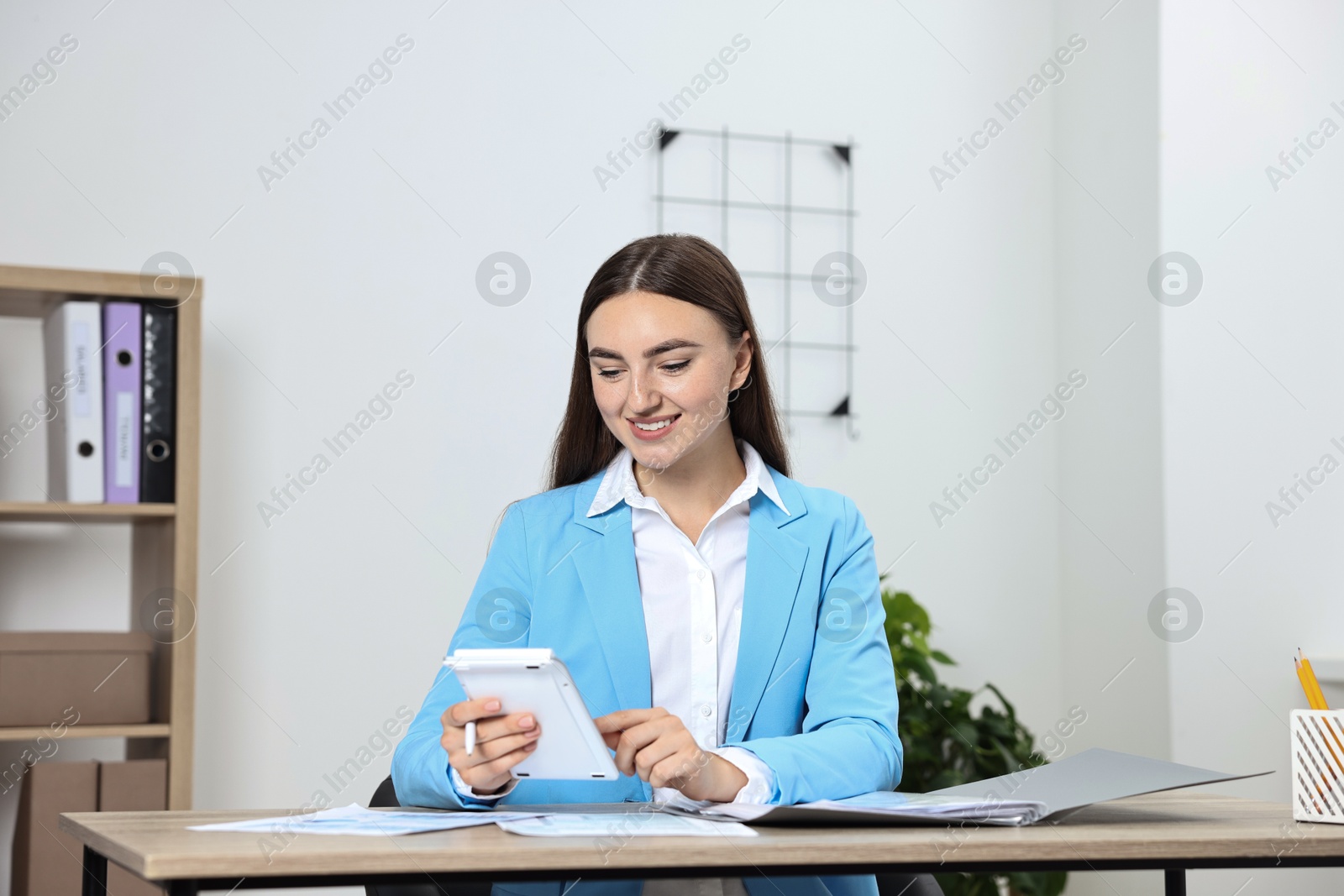 Photo of Budget planning. Young woman with papers using calculator at wooden table in office