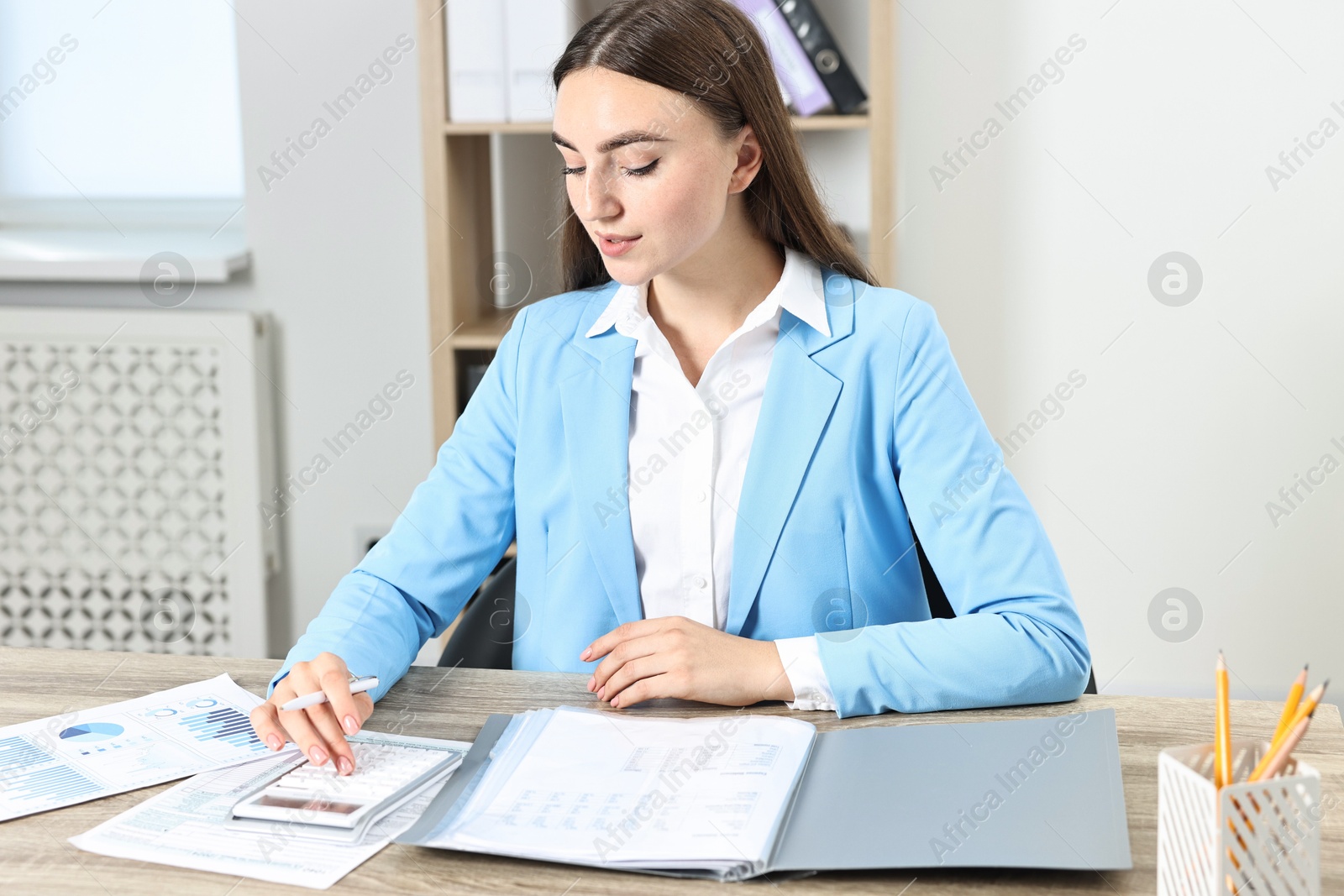 Photo of Budget planning. Beautiful young woman with papers using calculator at wooden table indoors