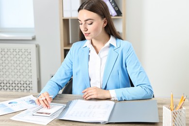 Budget planning. Beautiful young woman with papers using calculator at wooden table indoors