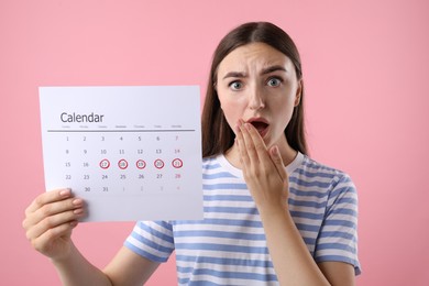 Photo of Emotional woman holding calendar with marked menstrual cycle days on pink background