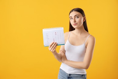 Photo of Woman holding calendar with marked menstrual cycle days on orange background, space for text