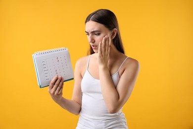 Photo of Woman holding calendar with marked menstrual cycle days on orange background