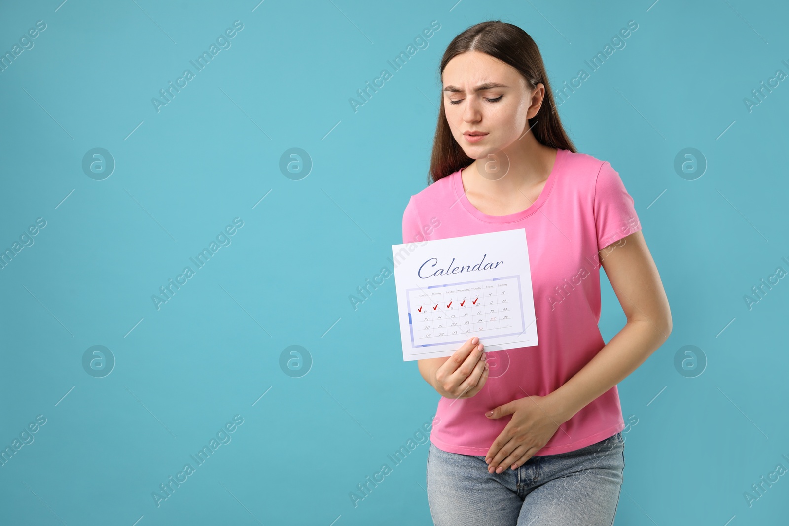 Photo of Woman holding calendar with marked menstrual cycle days and suffering from abdominal pain on light blue background, space for text