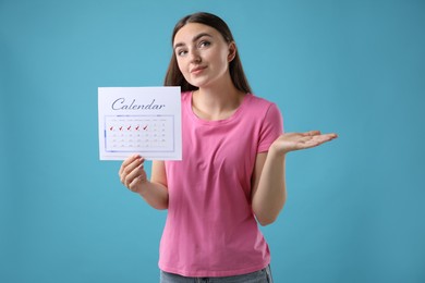 Photo of Woman holding calendar with marked menstrual cycle days on light blue background