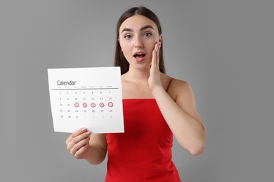 Woman holding calendar with marked menstrual cycle days on grey background