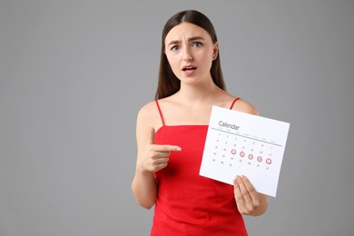 Woman holding calendar with marked menstrual cycle days on grey background, space for text