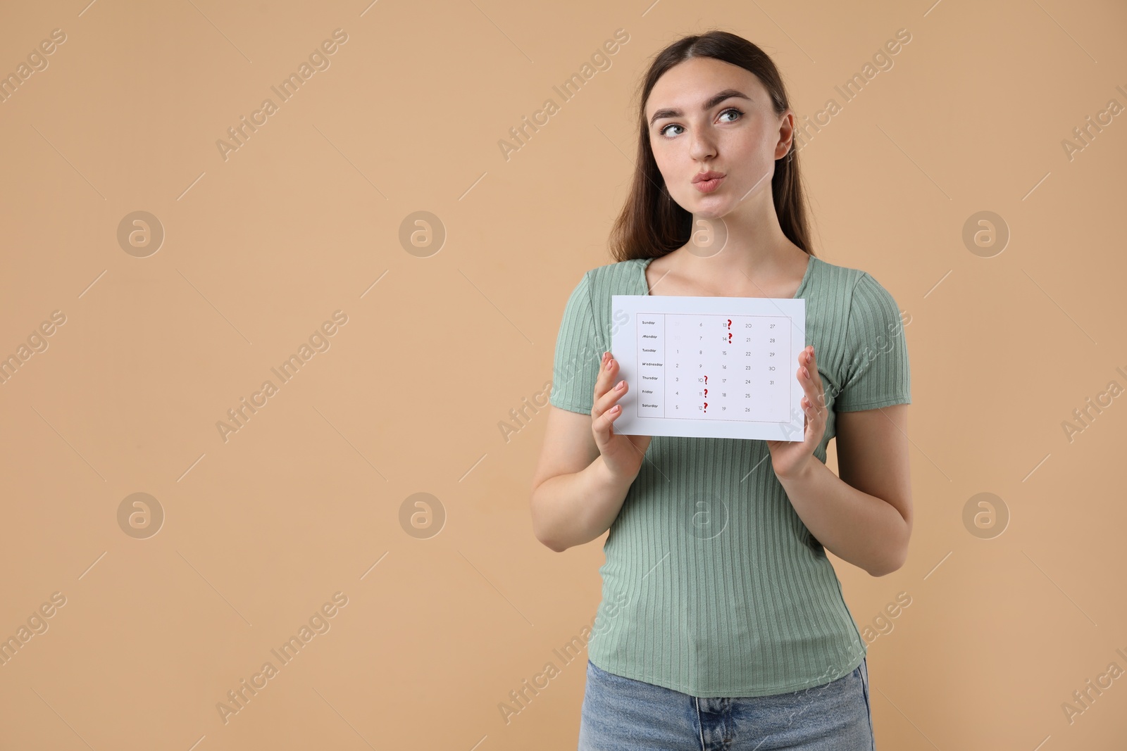 Photo of Woman holding calendar with marked menstrual cycle days on beige background, space for text