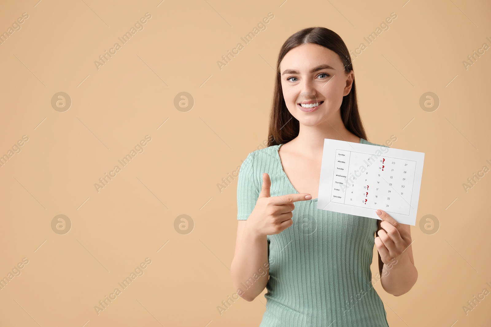 Photo of Woman holding calendar with marked menstrual cycle days on beige background, space for text