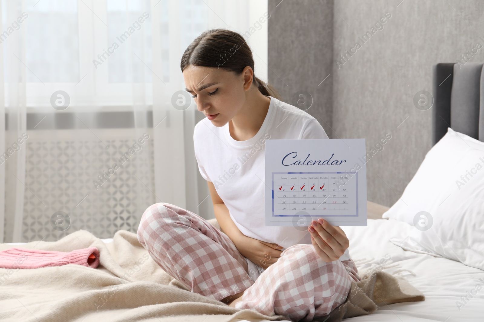 Photo of Woman holding calendar with marked menstrual cycle days on bed at home