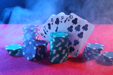 Photo of Poker chips and playing cards on pink table