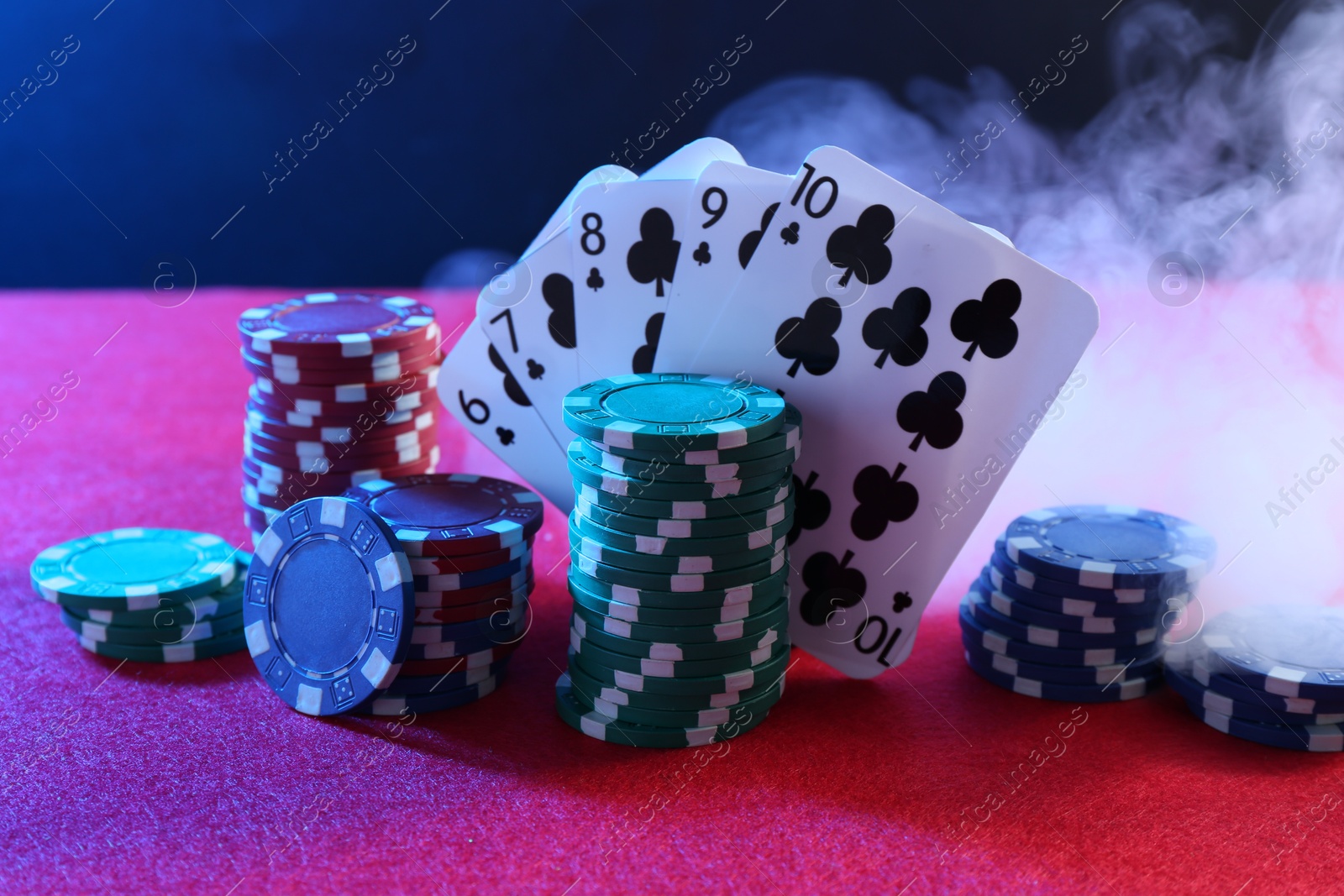 Photo of Poker chips and playing cards on pink table