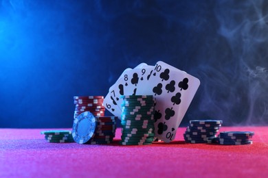 Photo of Poker chips and playing cards on pink table