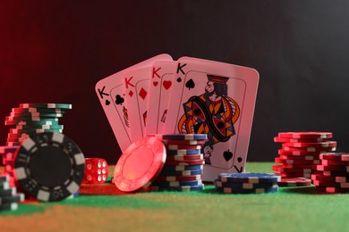 Photo of Poker chips, dice and playing cards on green table in neon lights, closeup