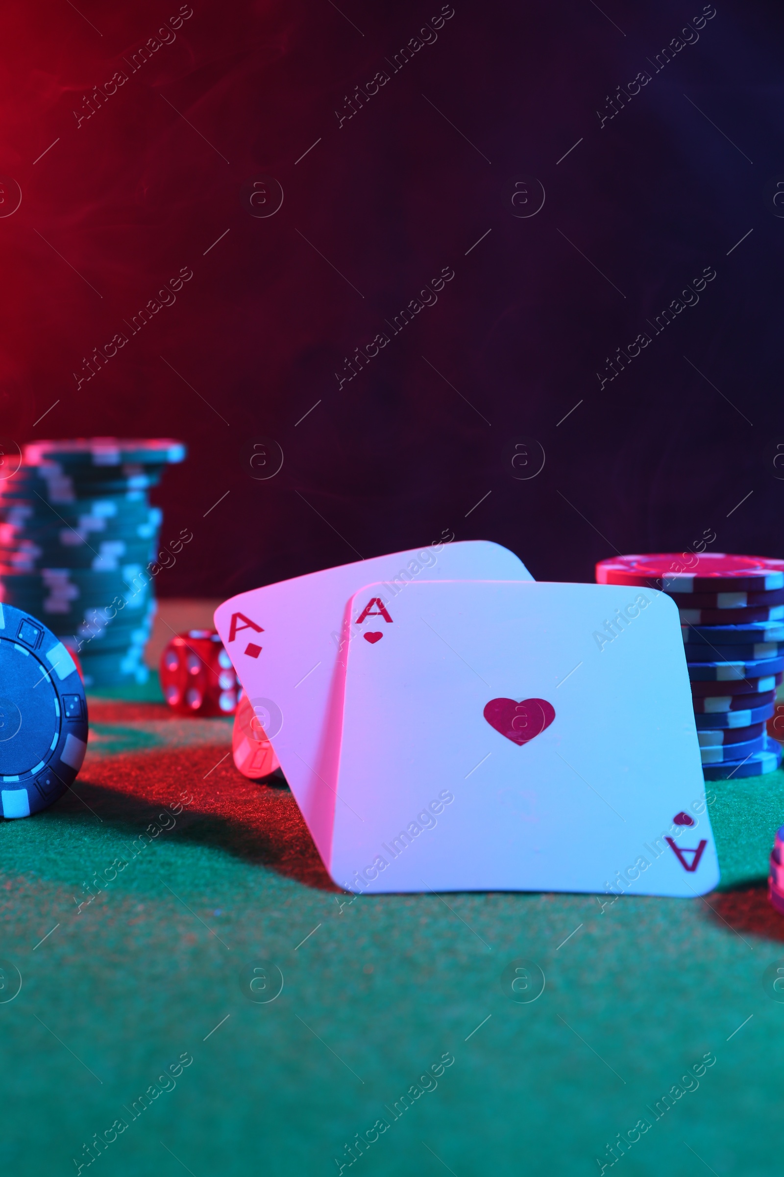 Photo of Poker chips and playing cards on green table in neon lights, closeup