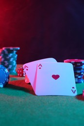 Photo of Poker chips and playing cards on green table in neon lights, closeup