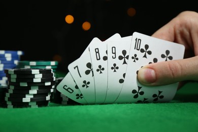 Photo of Poker game. Woman with playing cards and chips at green table, closeup