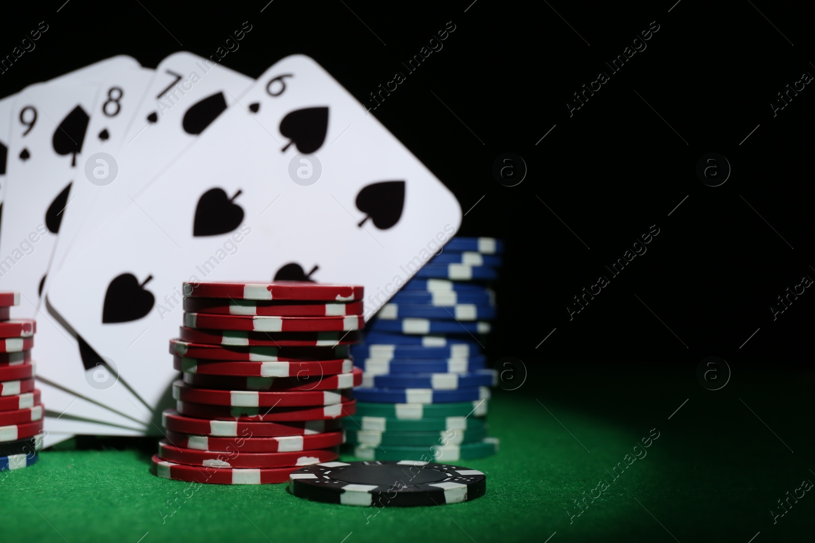 Photo of Poker chips and playing cards on green table, closeup. Space for text