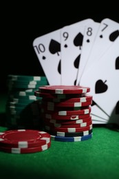 Photo of Poker chips and playing cards on green table, closeup