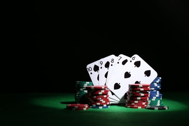 Photo of Poker chips and playing cards on green table, space for text