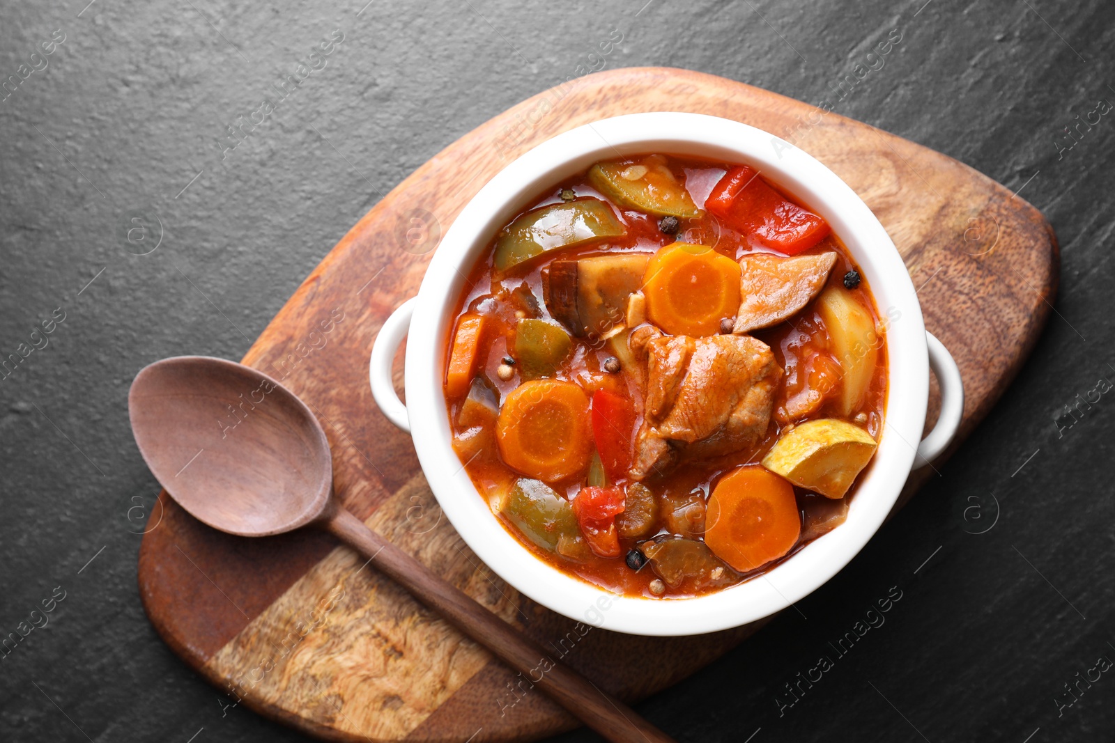 Photo of Delicious stew with vegetables in bowl served on gray textured table, top view