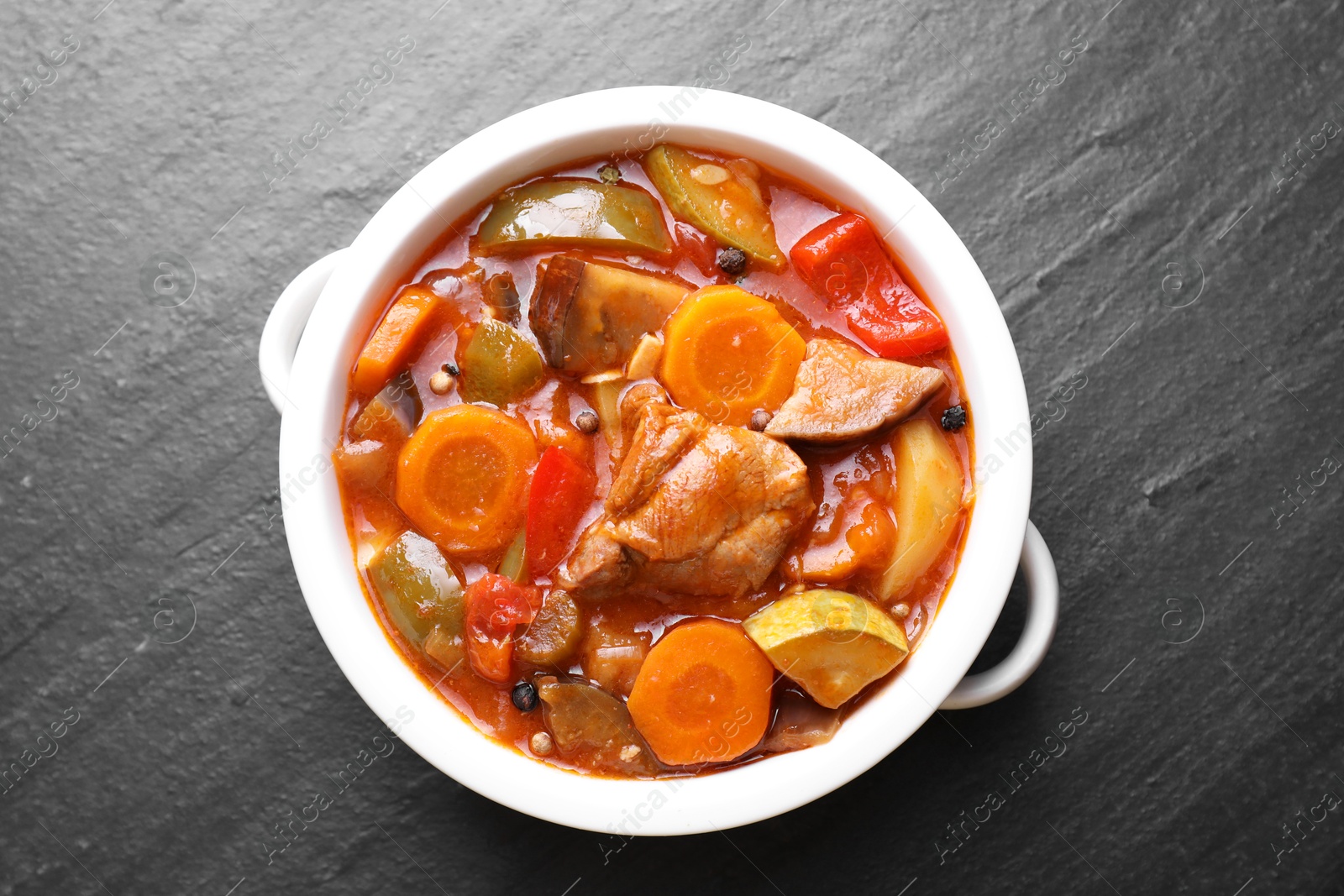 Photo of Delicious stew with vegetables in bowl on gray textured table, top view