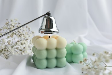 Photo of Stylish bubble candles, snuffer and gypsophila flowers on white cloth, closeup