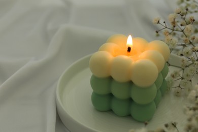 Photo of Stylish bubble candle and gypsophila flowers on white cloth, closeup. Space for text