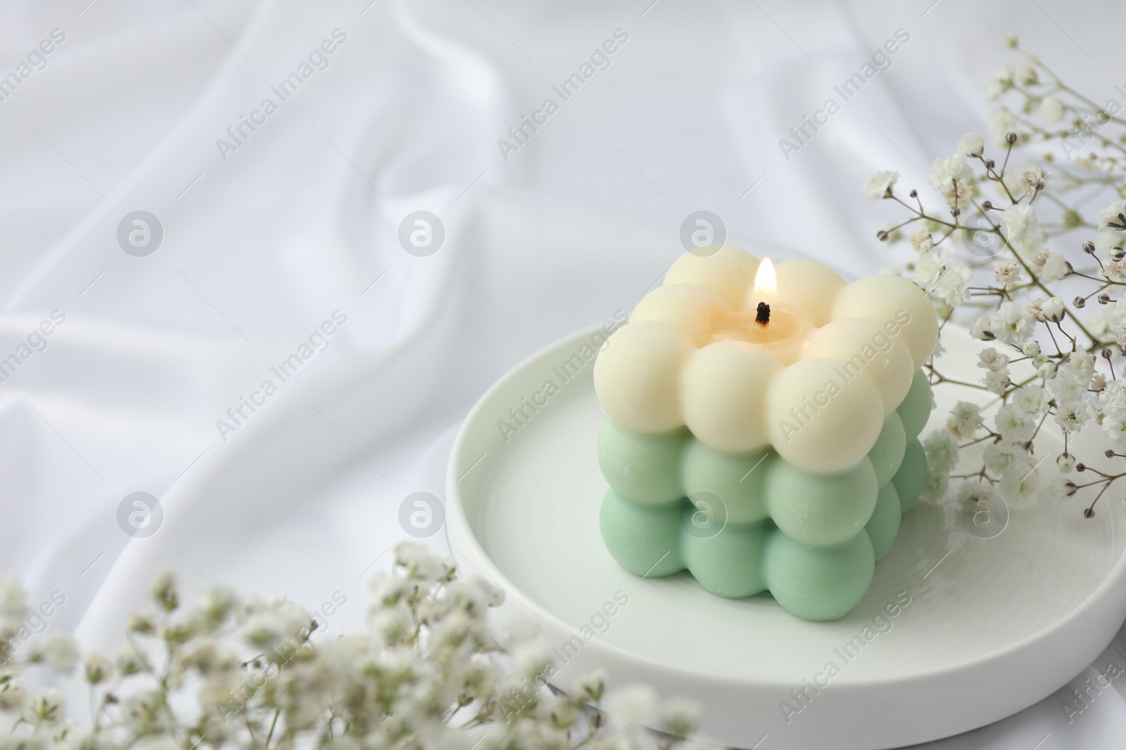 Photo of Stylish bubble candle and gypsophila flowers on white cloth, closeup. Space for text