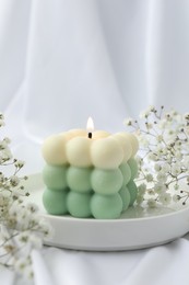 Photo of Stylish bubble candle and gypsophila flowers on white cloth, closeup