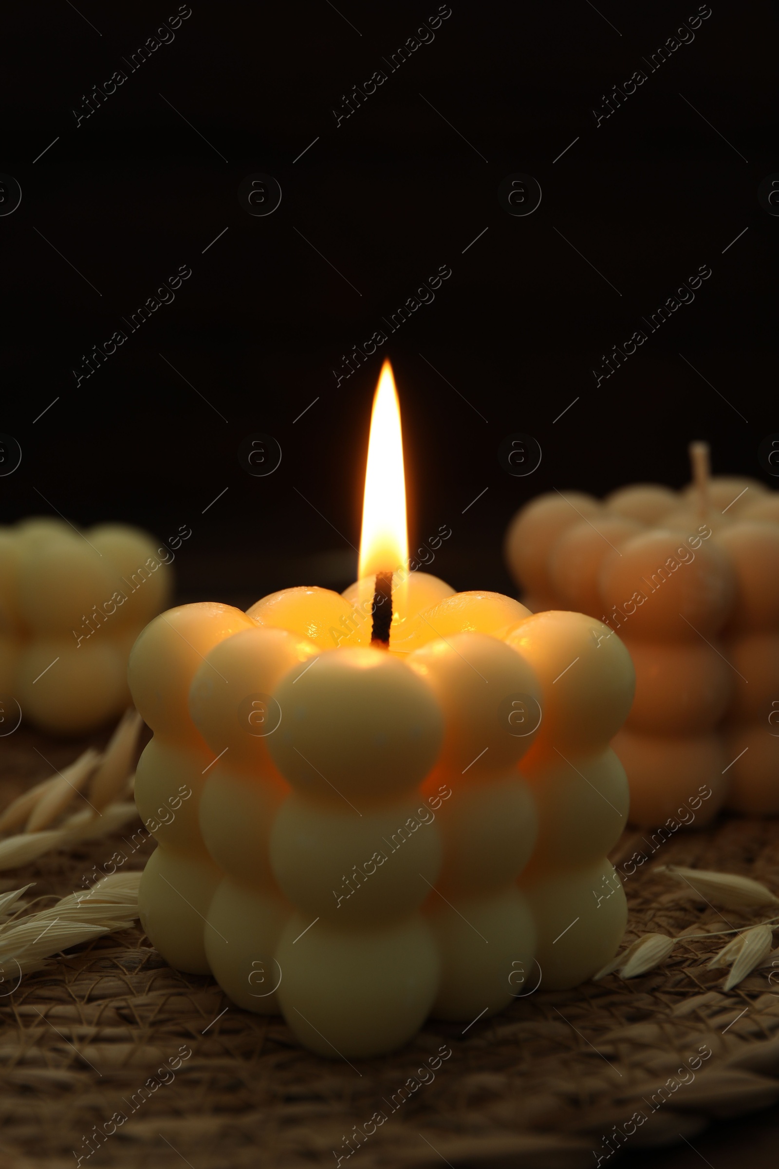 Photo of Burning bubble candle on wicker mat against black background, closeup