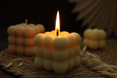 Photo of Burning bubble candle on wicker mat against black background, closeup