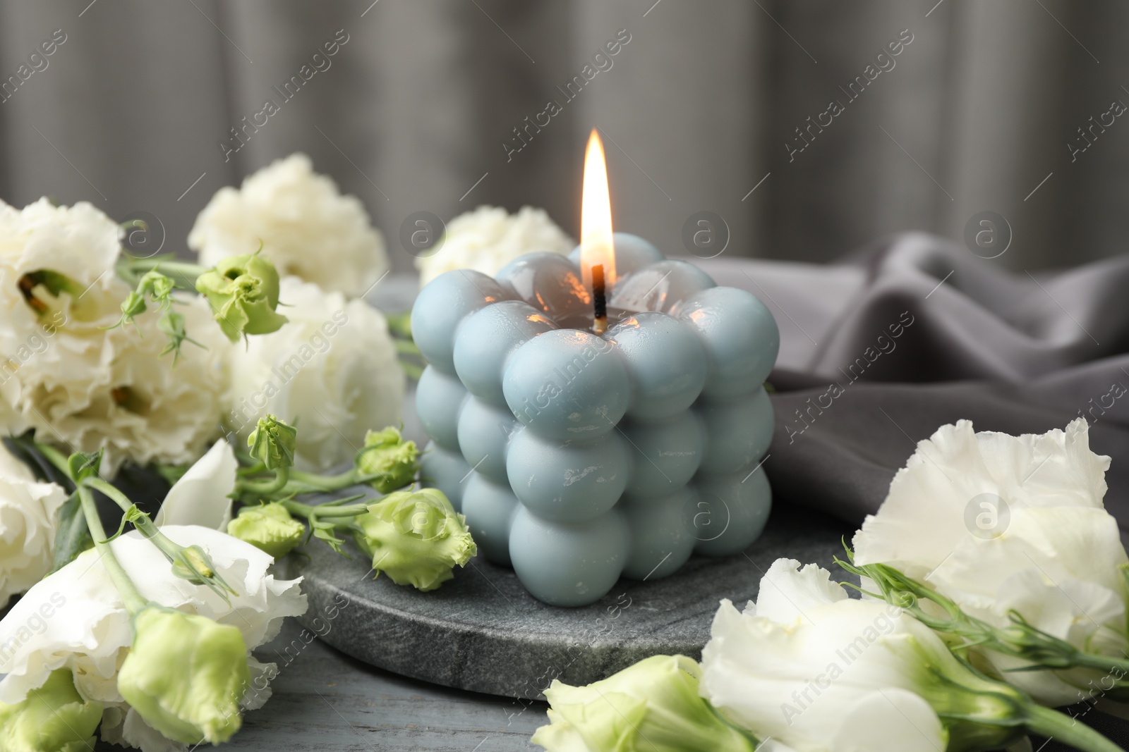 Photo of Burning bubble candle and beautiful flowers on table, closeup