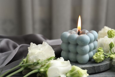 Photo of Burning bubble candle and beautiful flowers on table, closeup