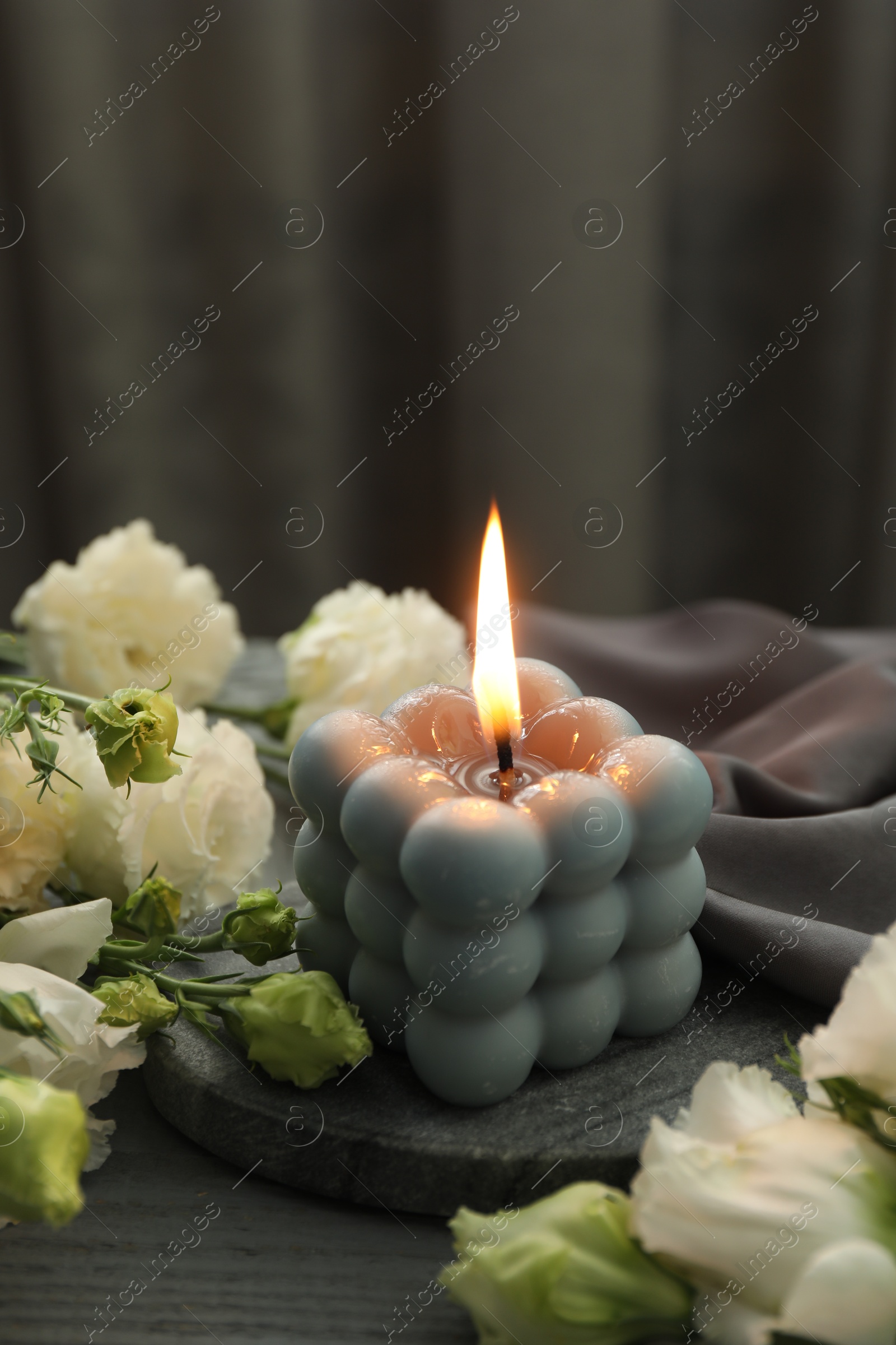 Photo of Burning bubble candle and beautiful flowers on grey wooden table, closeup