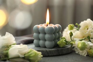 Photo of Burning bubble candle and beautiful flowers on grey wooden table, closeup