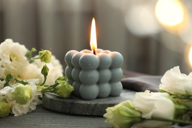 Photo of Burning bubble candle and beautiful flowers on grey wooden table, closeup