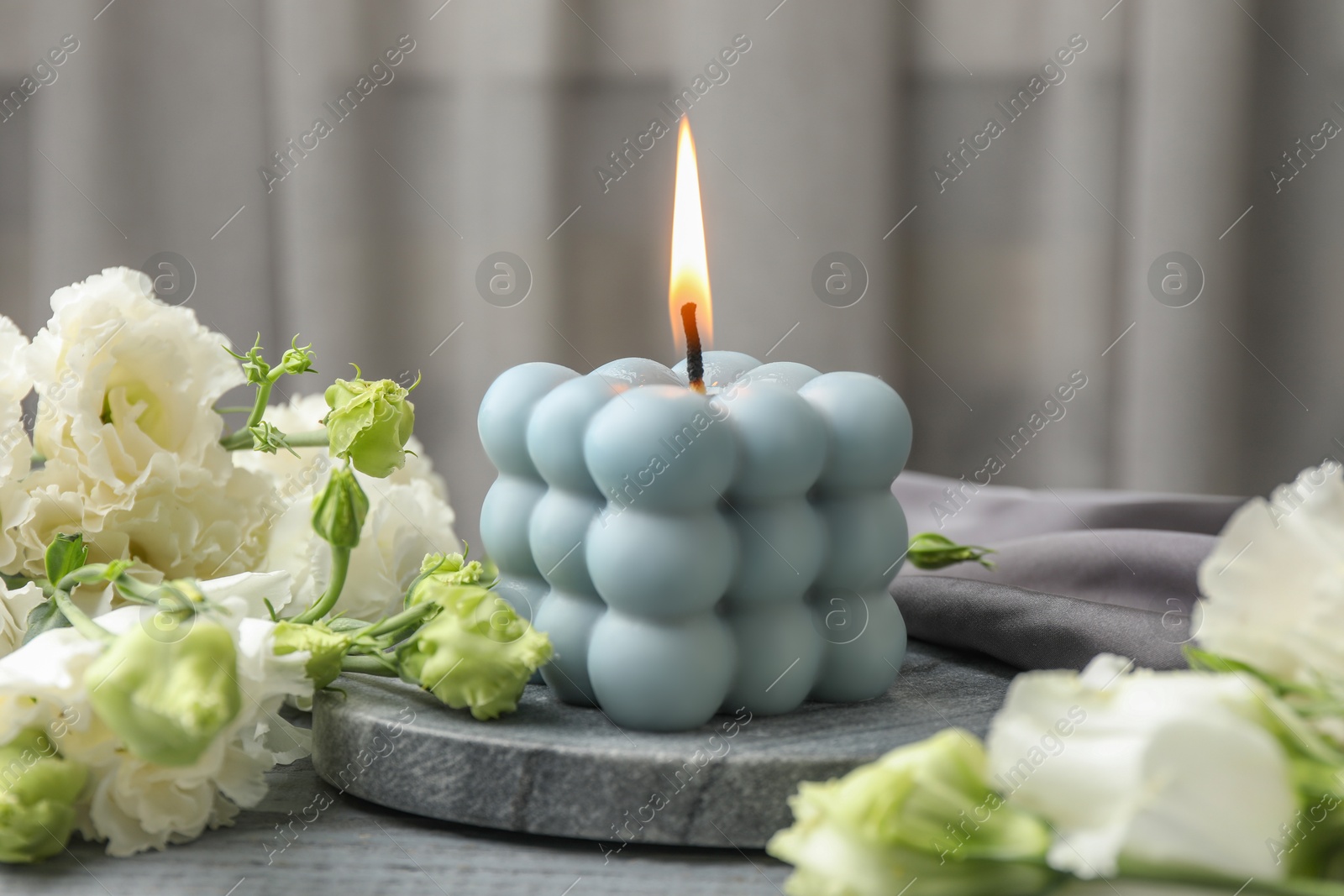 Photo of Burning bubble candle and beautiful flowers on grey wooden table, closeup