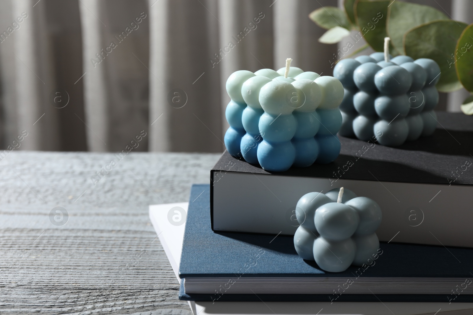 Photo of Stylish bubble candles and stack of books on grey wooden table, closeup. Space for text